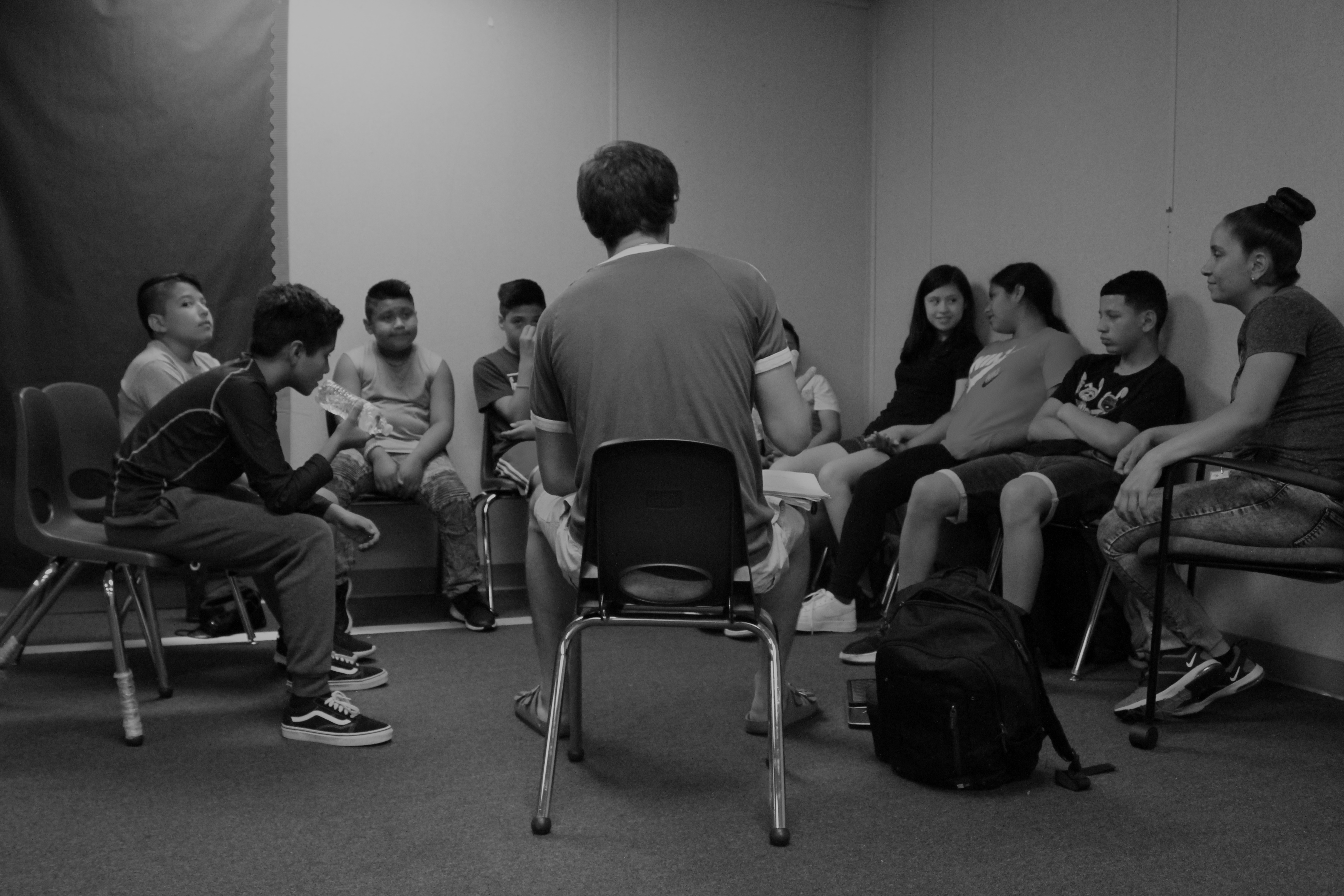 Black & white image of children seated in circle during songwriting workshop with We Amplify Voices