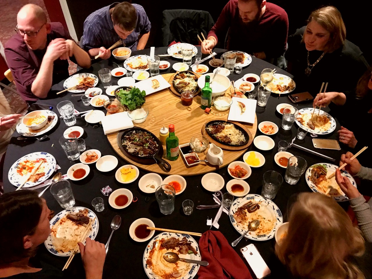 Table surrounded by diners and completely covered in various Korean dishes and saucebowls