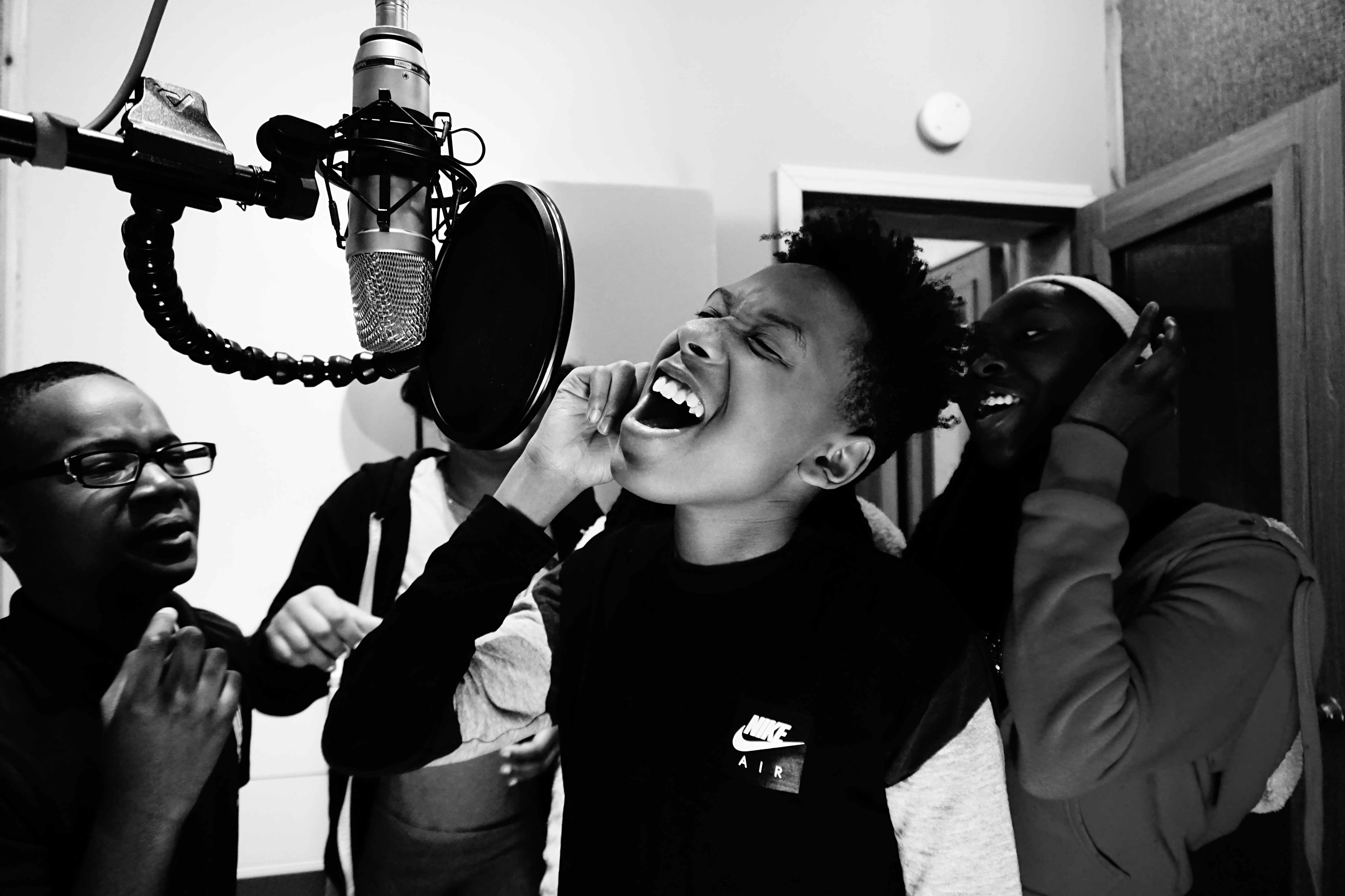 Black & white photo of children singing into microphone in recording studio booth