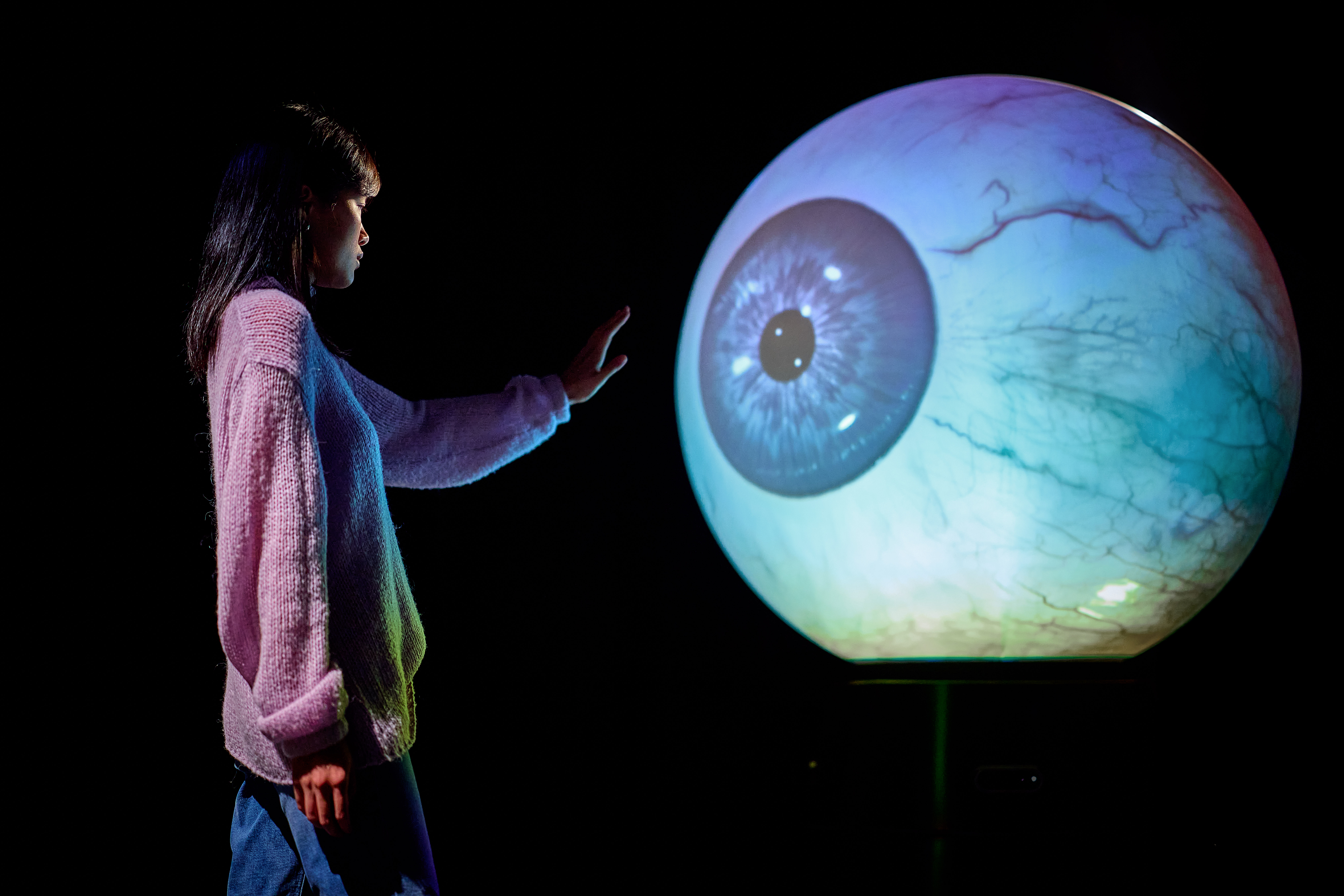 Woman reaching out to touch large interactive eyeball at Prototype Museum