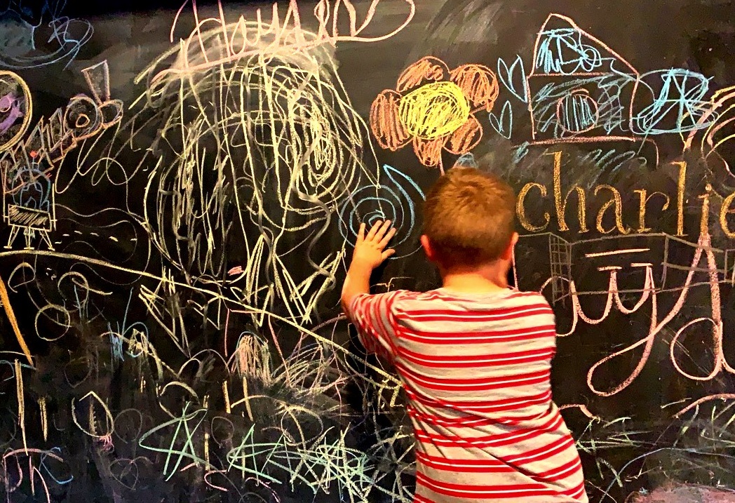 Young child drawing on chalkboard wall