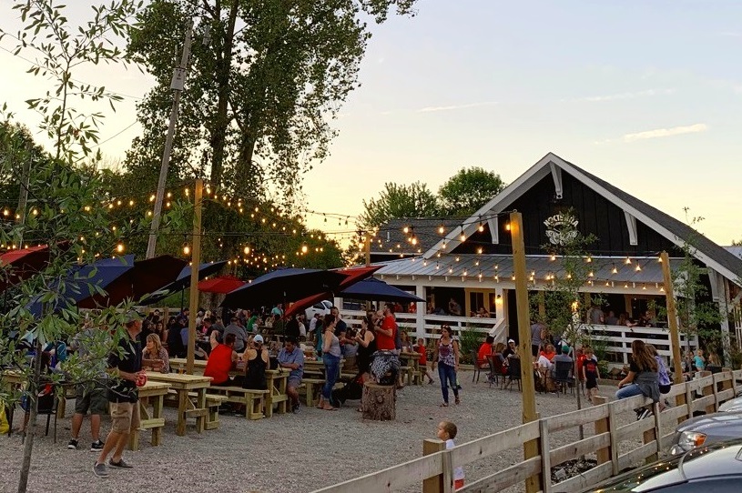 Outdoor patio decked with string lights, umbrellas and benches under sunset sky outside Nocterra Brewing