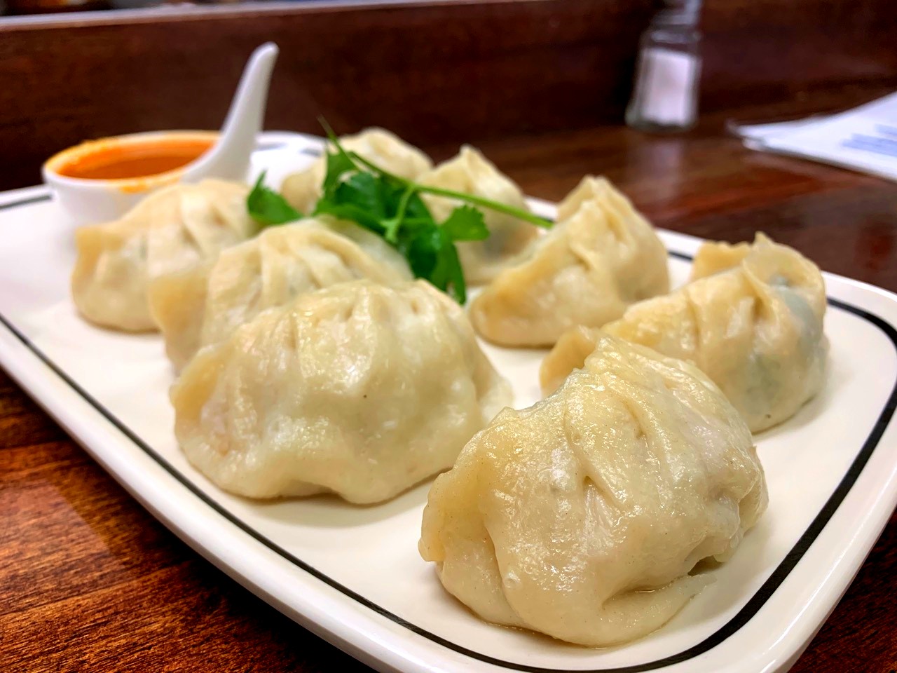 Dumplings on white plate with sauce and herb garnish at Momo Ghar restaurant