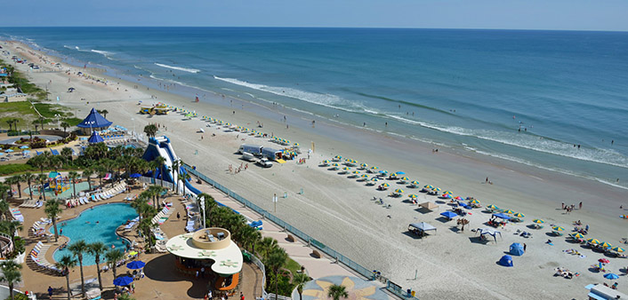 An aerial view of Daytona Beach with bright blue water and blue and yellow umbrellas