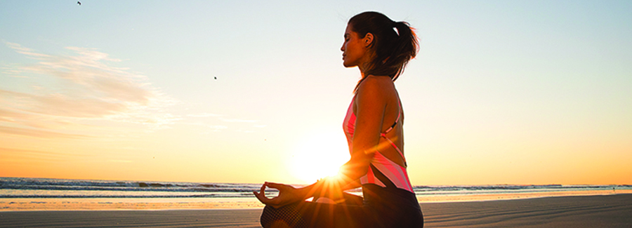 A woman sits in a yogic lotus position on Daytona Beach at sunrise.