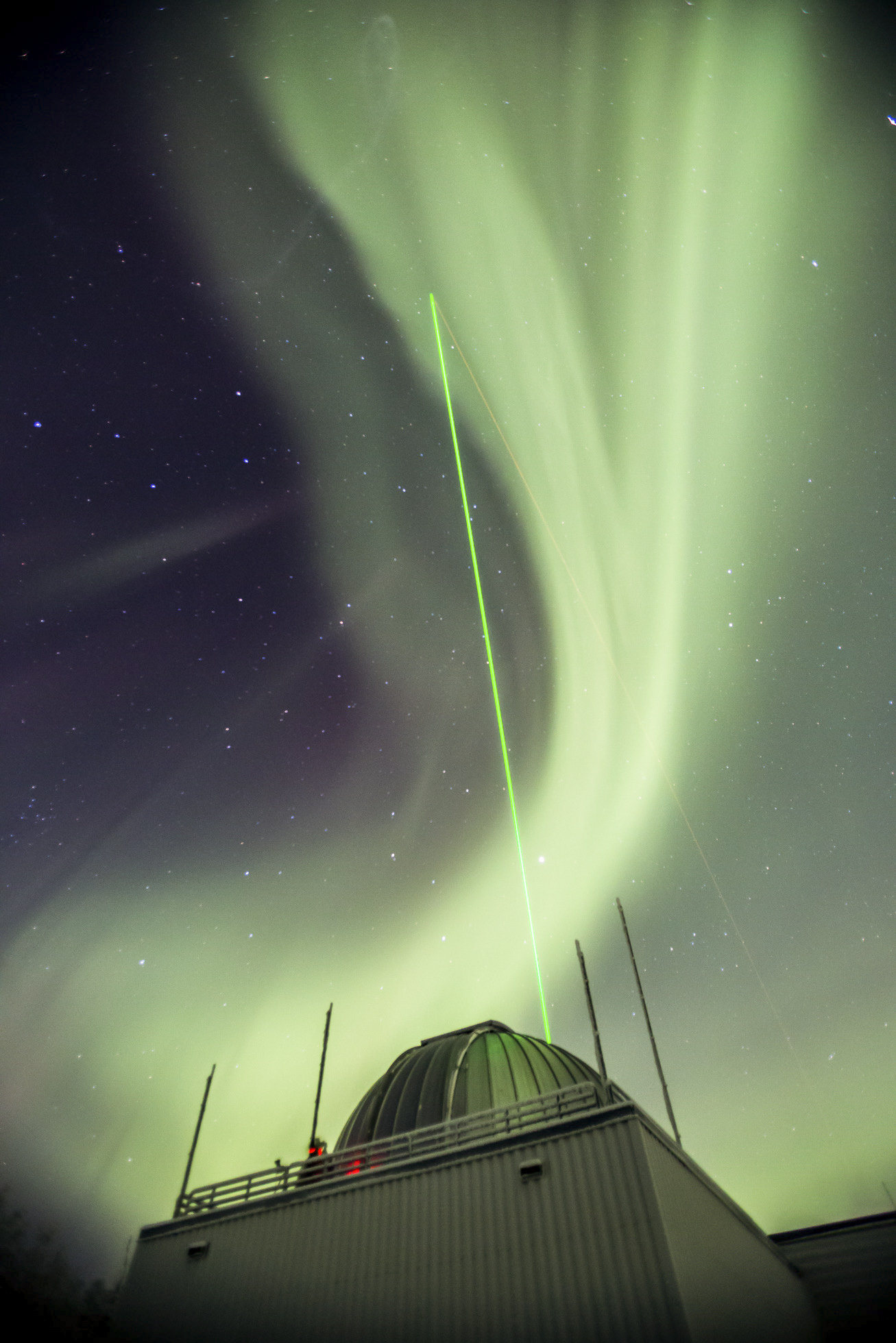 a green laser beam pointing into aurora-filled sky