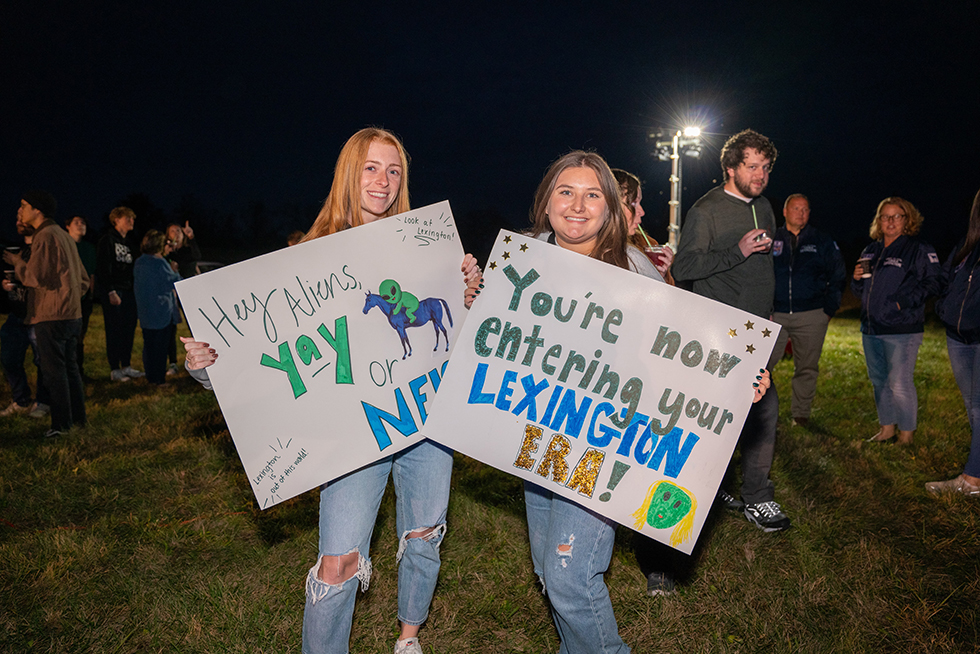 Two girls cheerfully holding signs welcoming aliens