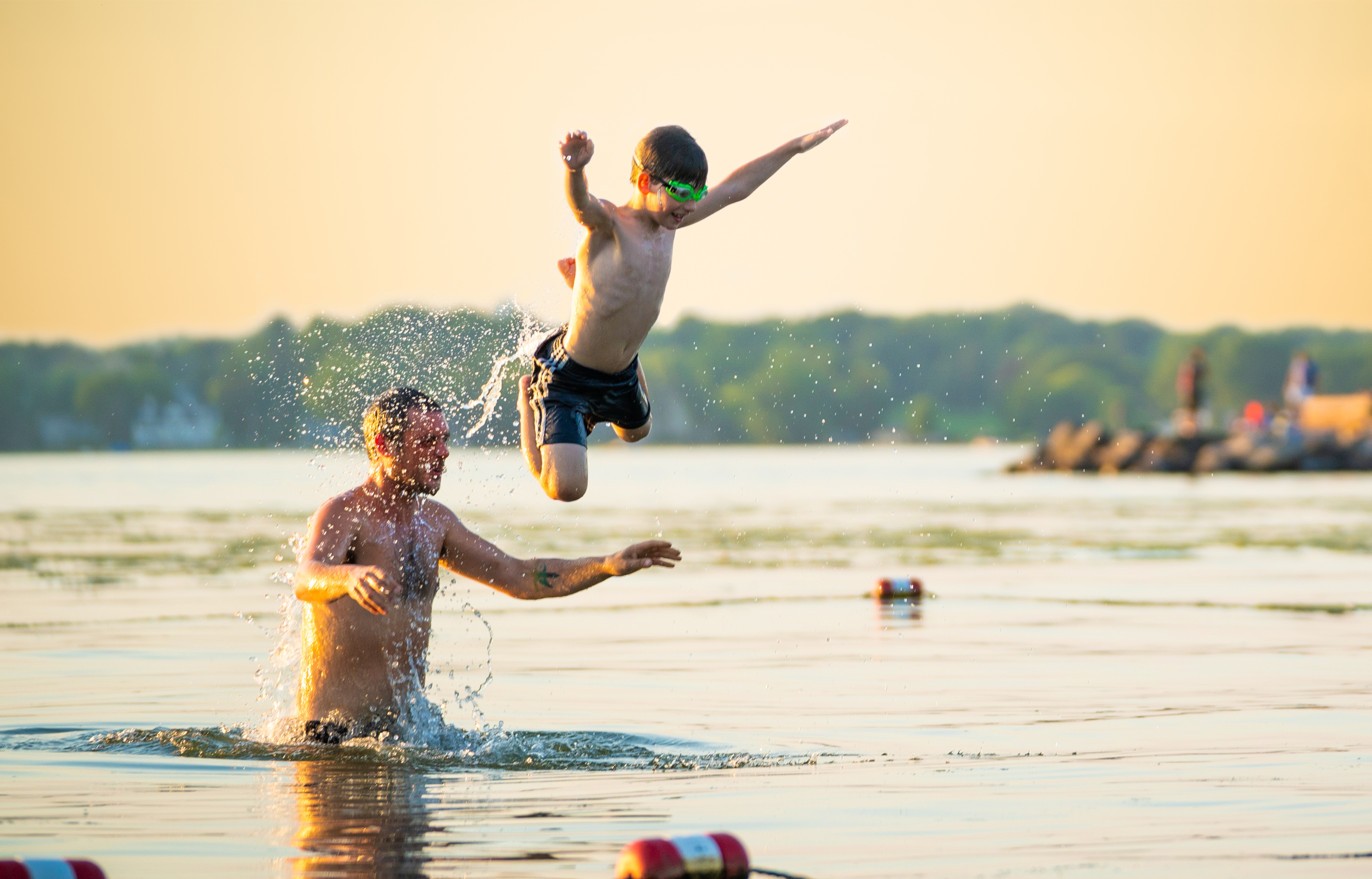 A child jumps off a man's shoulders into the water