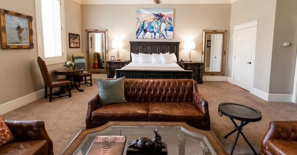 Hotel room with a bed, couch, side tables, and historic art on the walls.