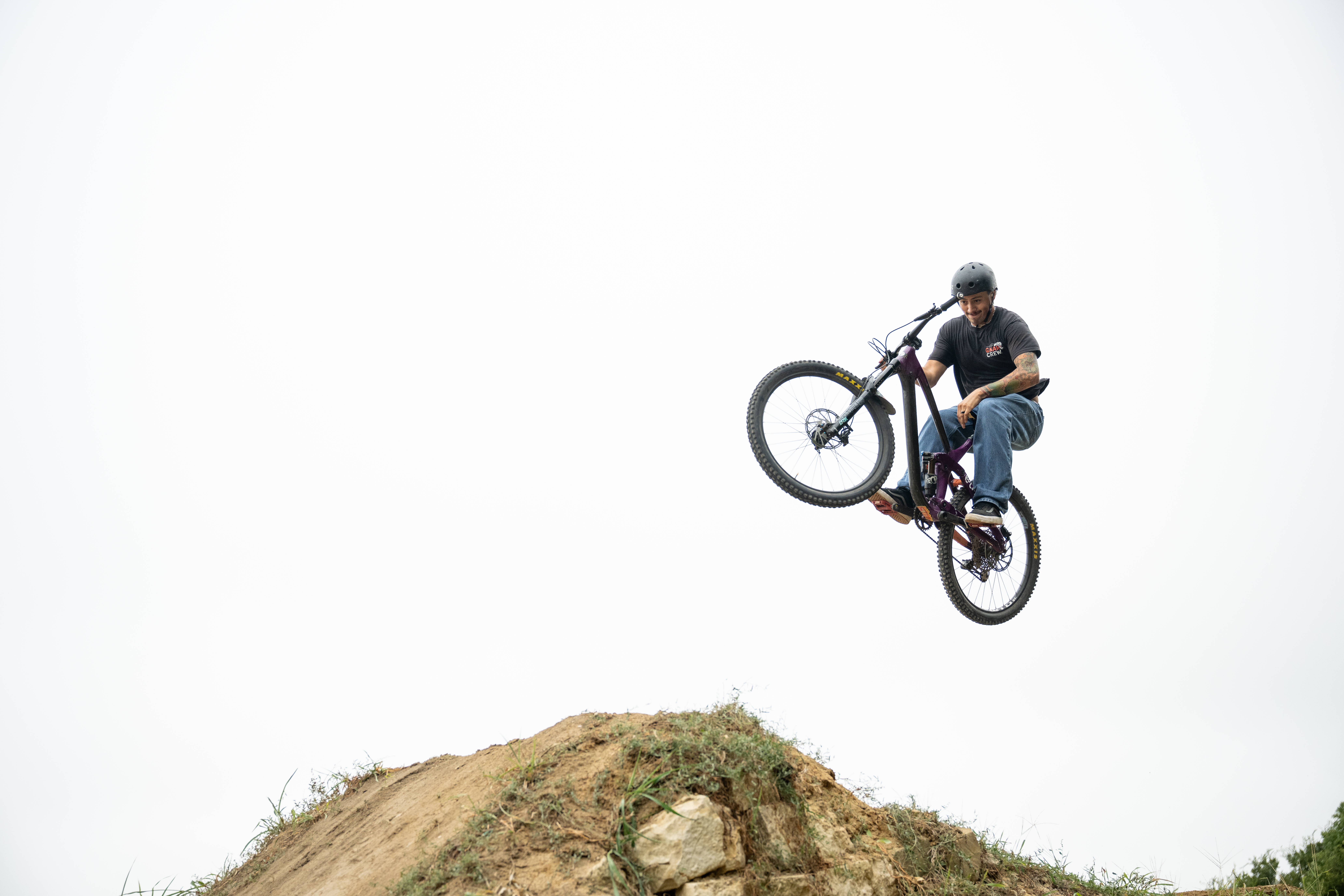 Young man on a mountain bike wearing a black shirt, blue jeans, and a black helmet.