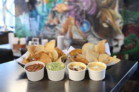 two baskets of chips in front of artwork on wall with cups of salsa, guacamole, queso at agave and rye in covington ky