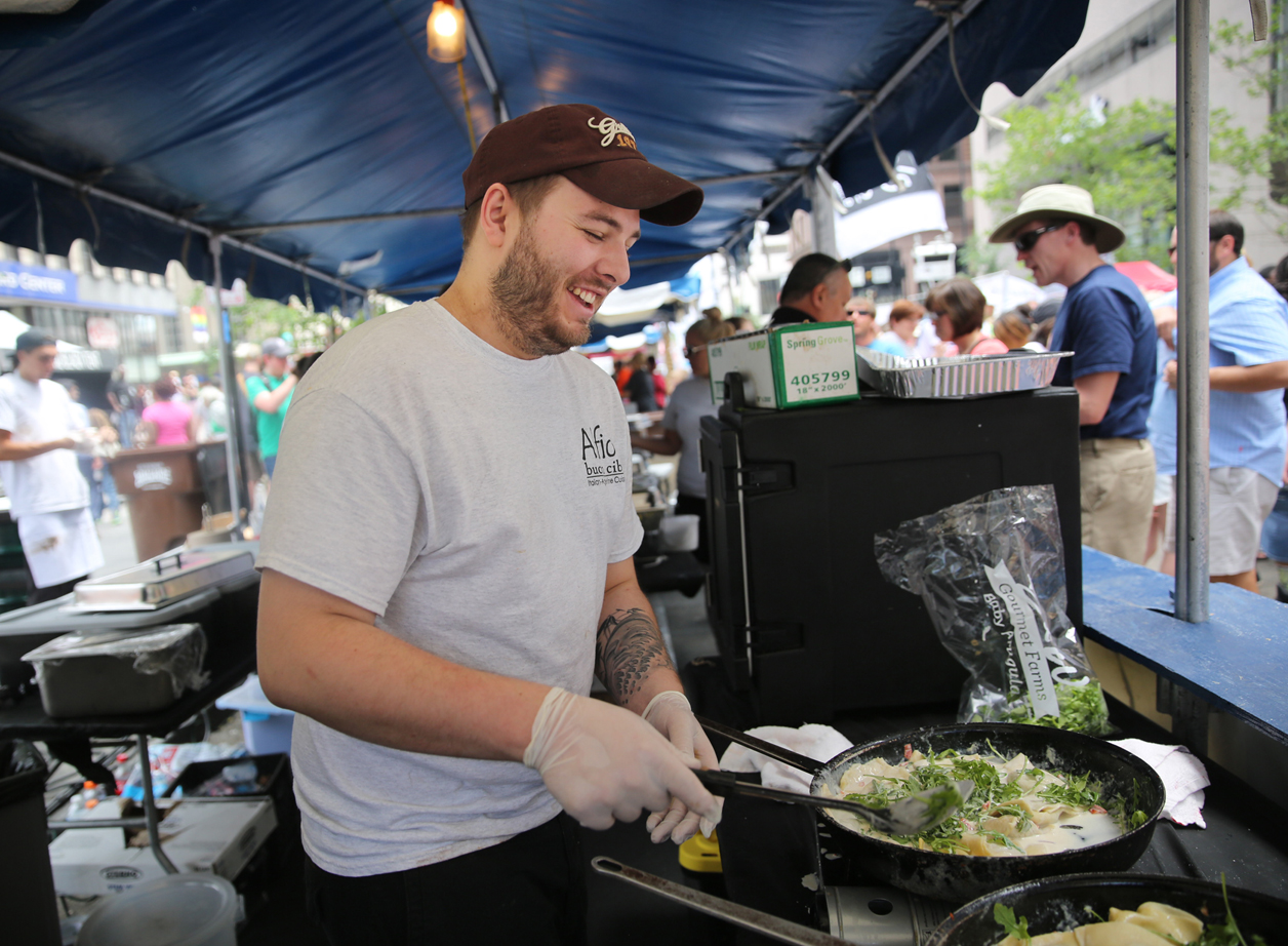 smiling man in ball cap cooking food in a skillet during taste of cincinnati on fountain square memorial day weekend