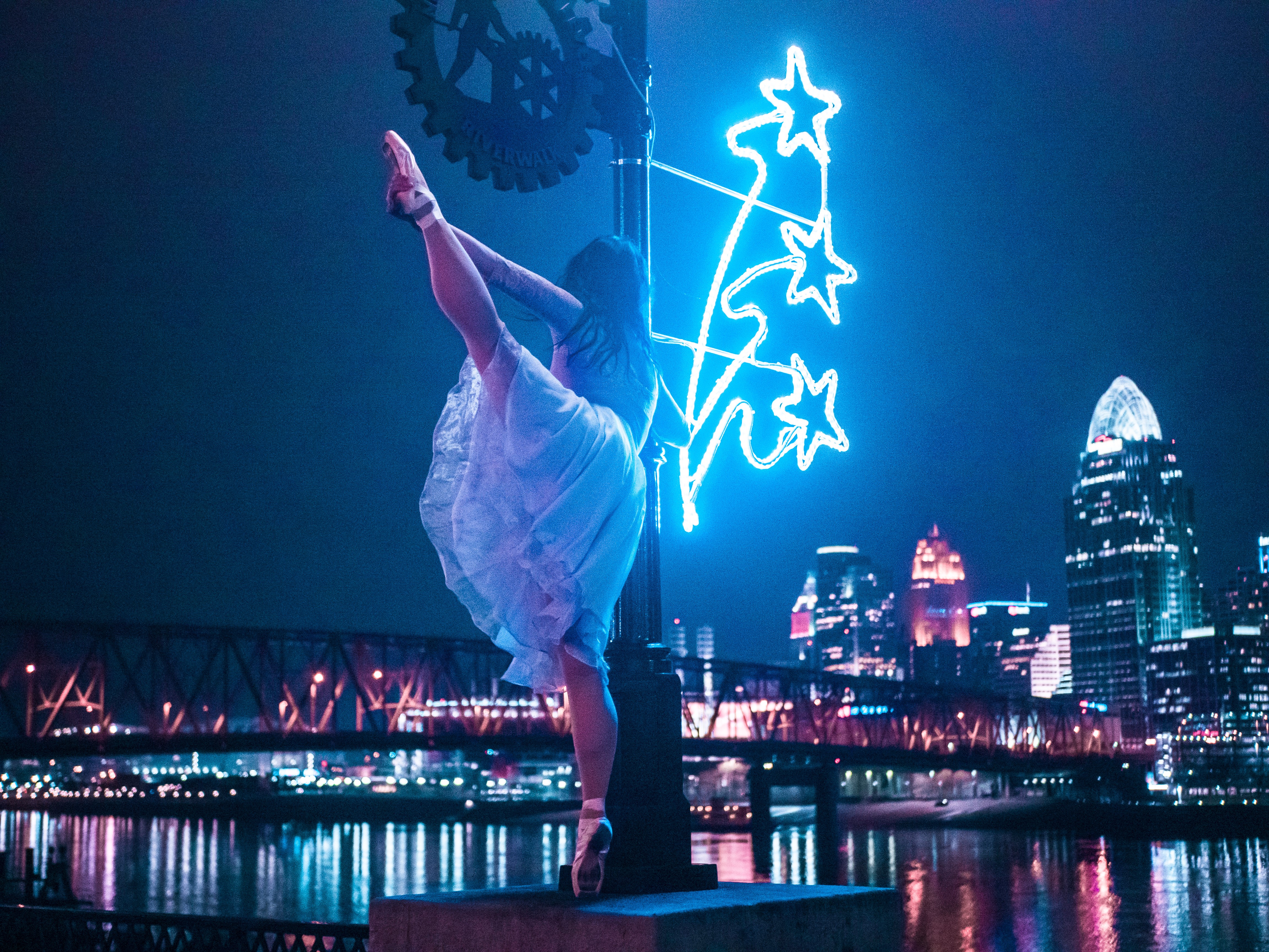 A ballerina in white dancing on Newport on the Levee with the Cincinnati skyline and Ohio river in the background