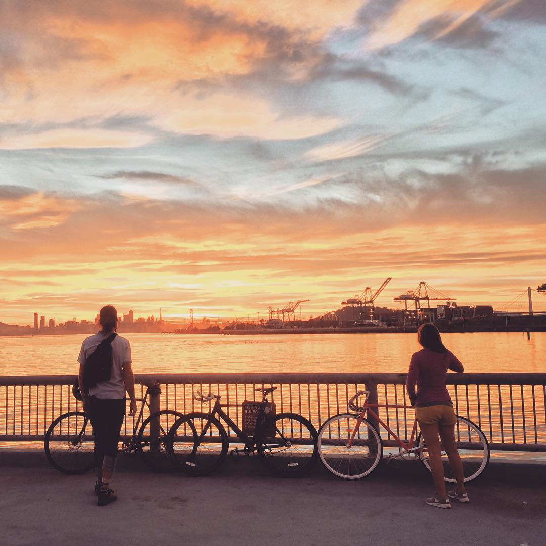 Man and woman with bicycles at Middle Harbor Shoreline Park at sunset
