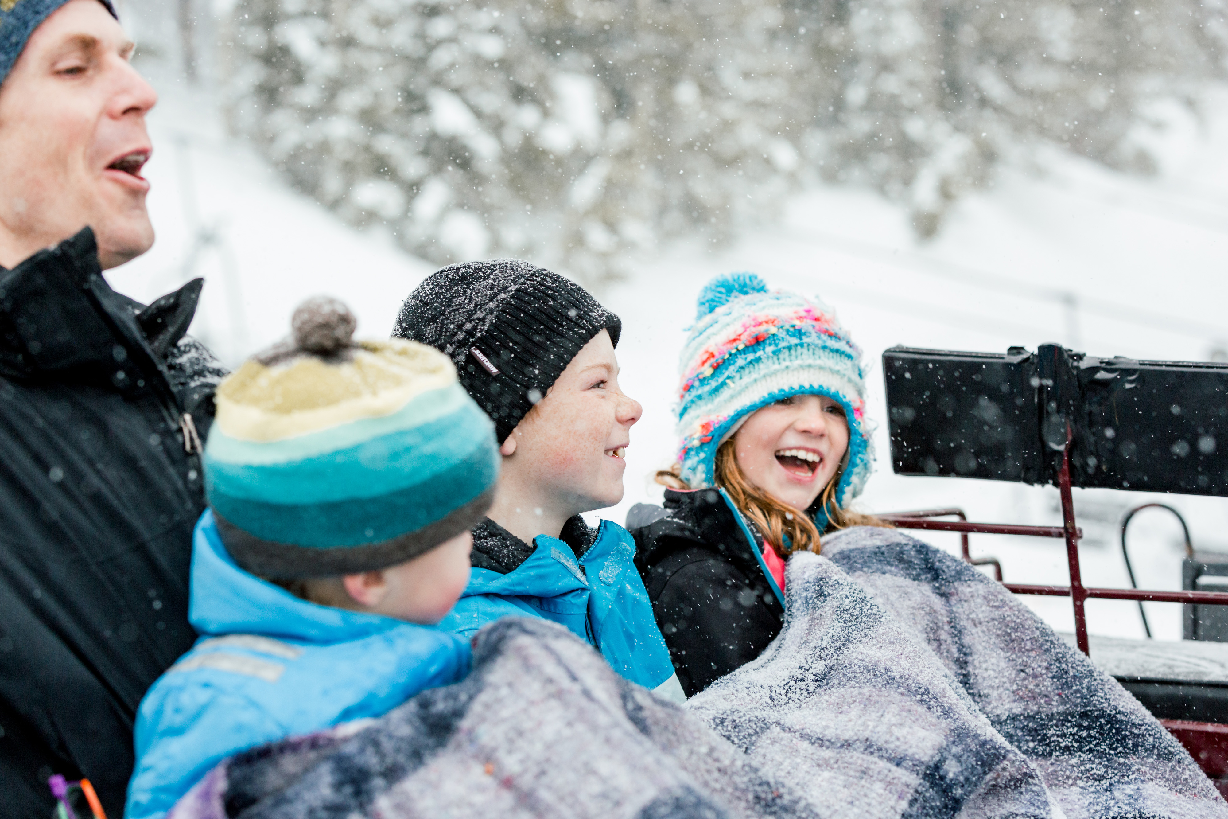 Dad and three children bundled up in a sleigh ride laughing