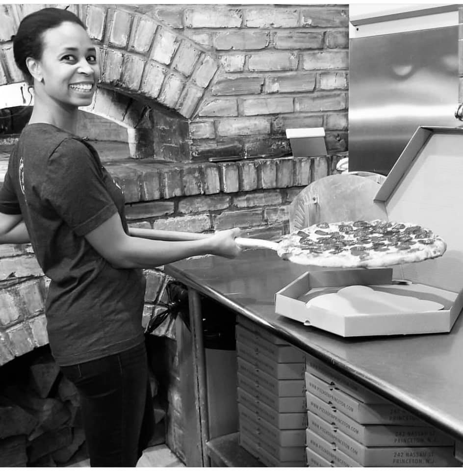 Smiling employee prepares a pepperoni pizza at Pizza Den
