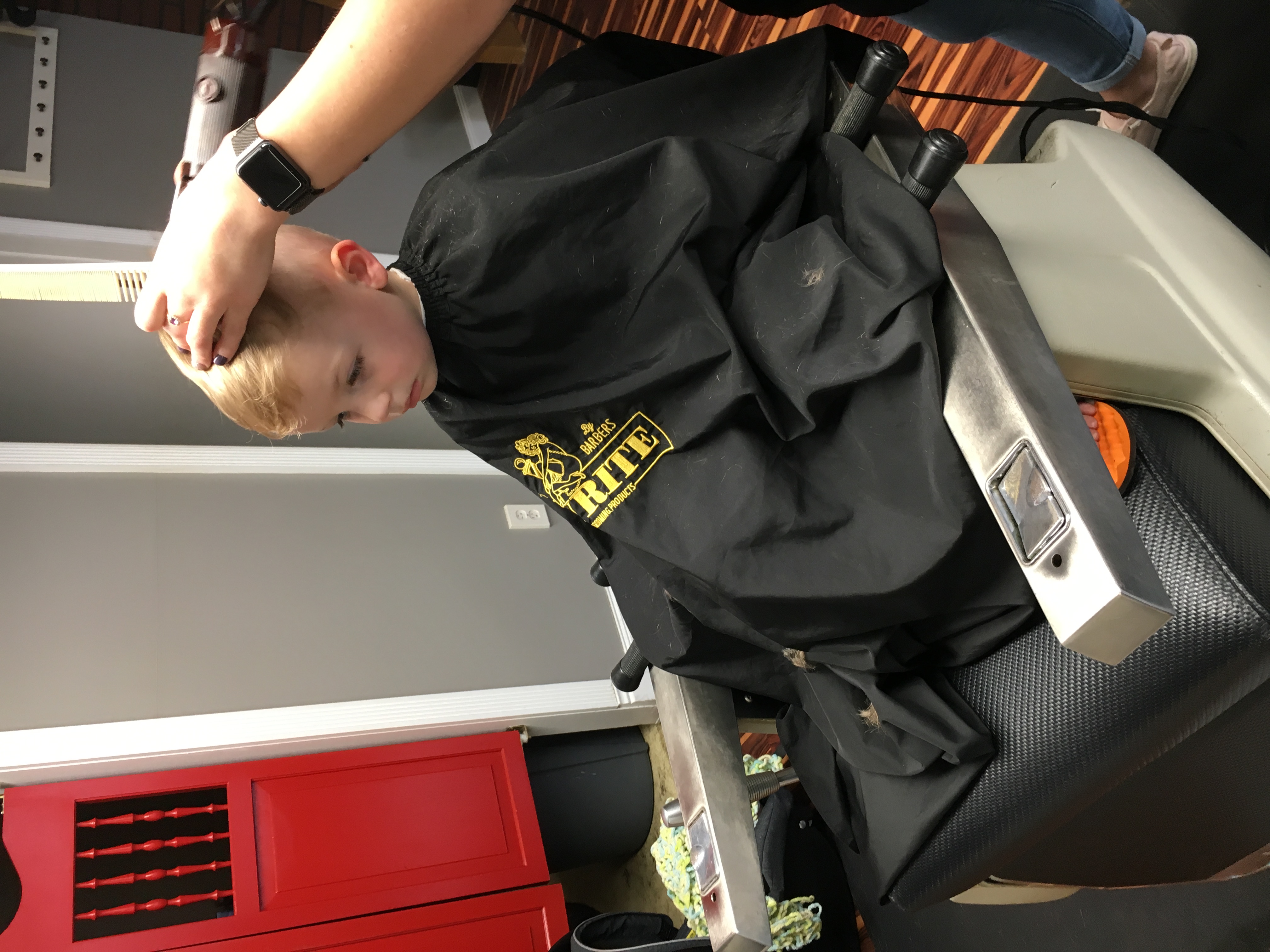 A young boy sits in a booster chair for a haircut