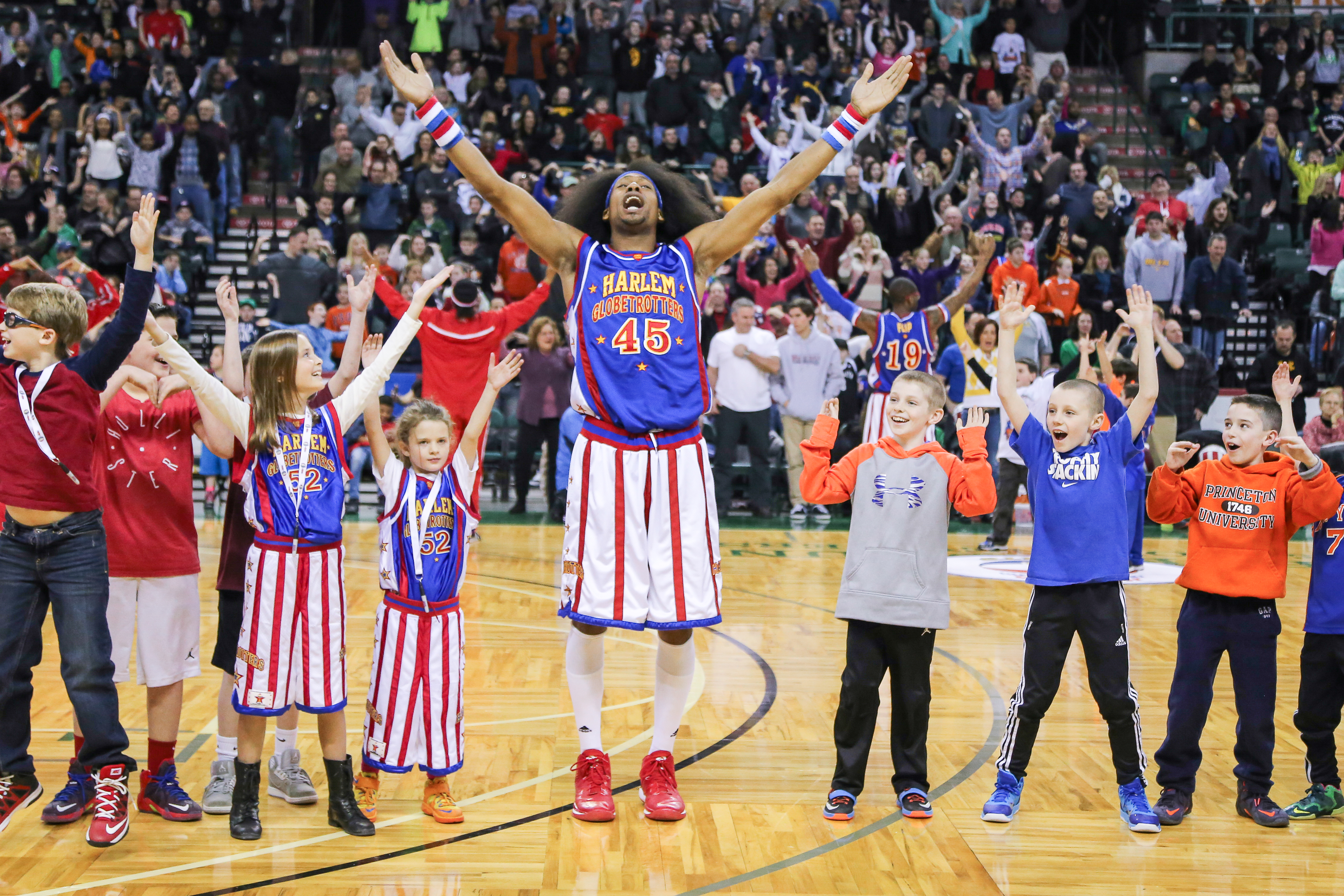A Harlem Globetrotter raising arms with a bunch of kids on the basketball court