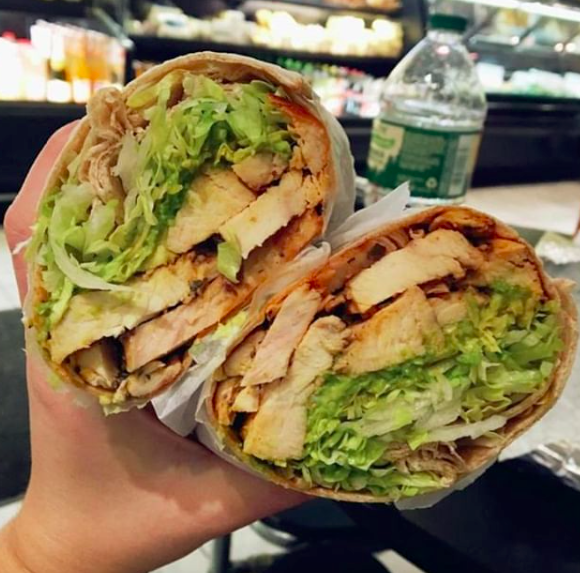 A lunch wrap is being held up filled with lettuce, chicken, avocado and more.