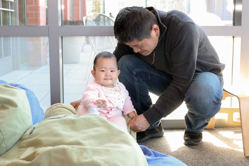 A man kneeling next to his infant daughter
