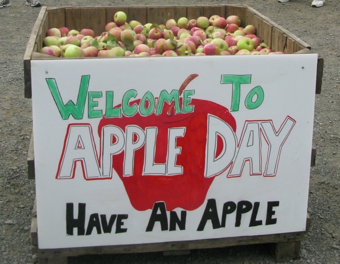 A bin of apples with a sign reading Welcome to Apple Day, Have an Apple