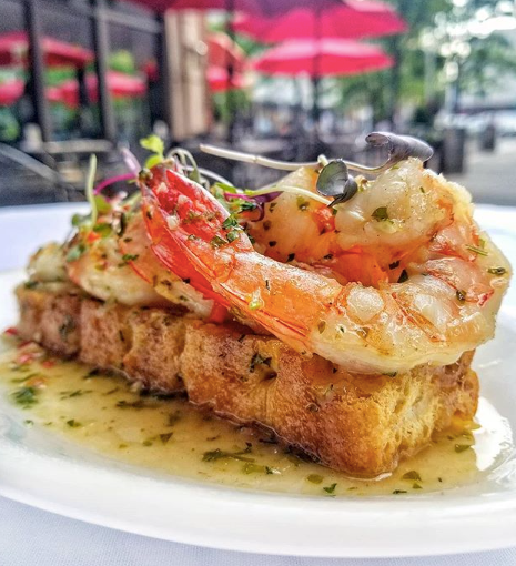 Seasoned shrimp sit on top of a crustini surrounded by oil and herbs