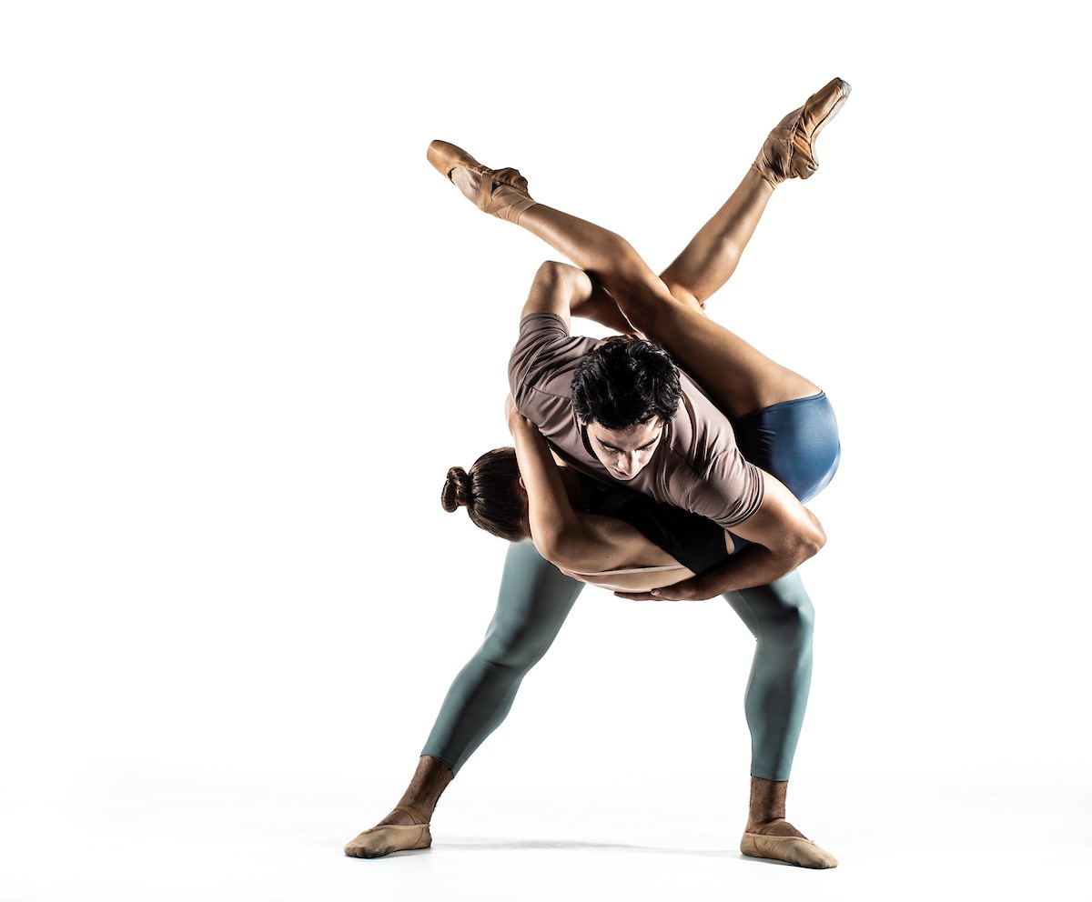 A man and woman performing an acrobatic dance in front of a white background.
