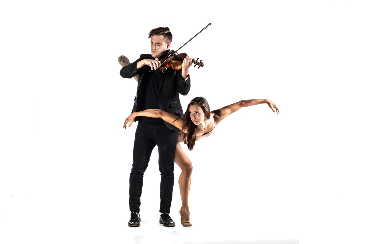 A man playing the violin while a woman dances around his back.