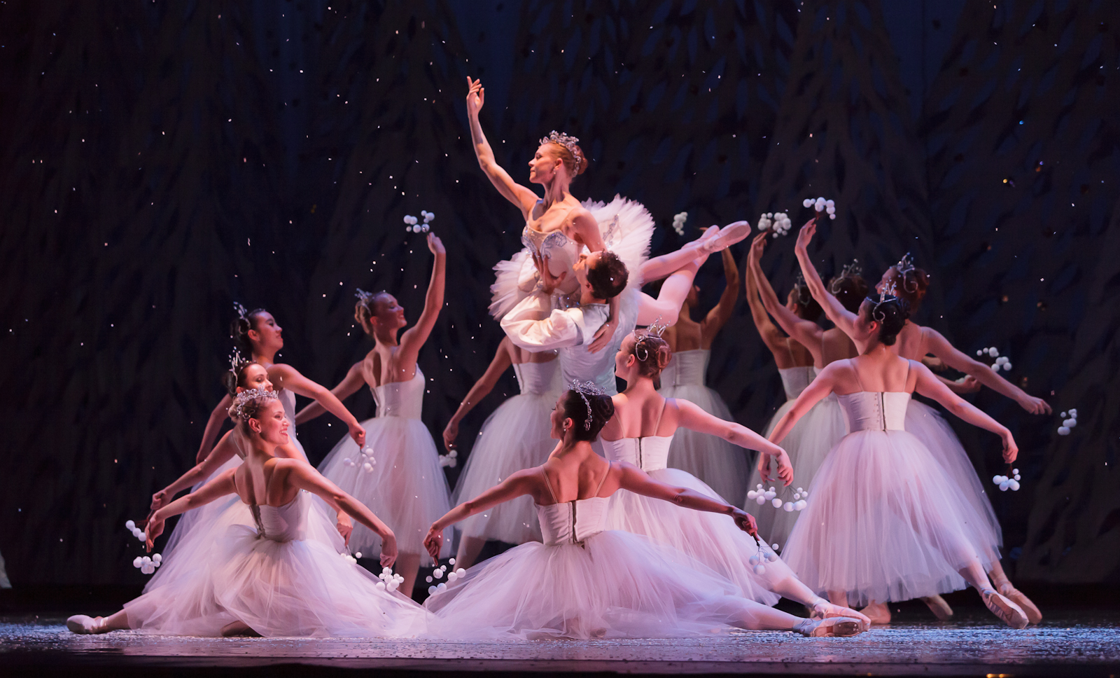More than a dozen women dressed in white surround the Sugar Plum Fairy, also dressed in white, whose held in the air by a man in white in the center of the circle.