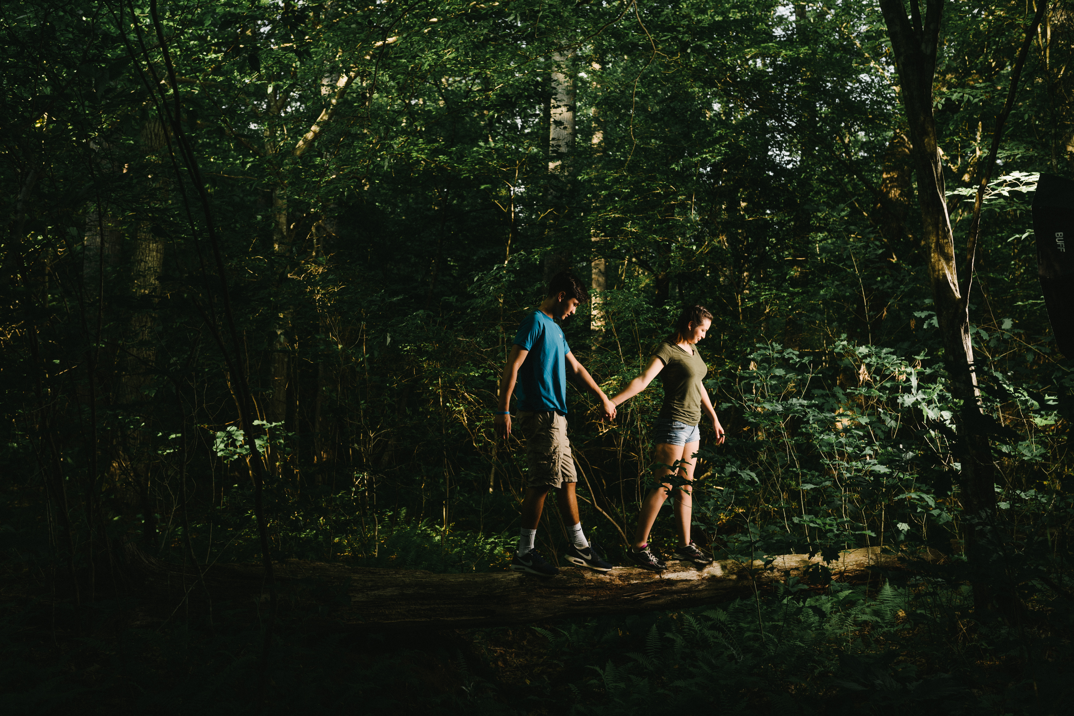 A young man and young woman walking on a log, holding hands in the forest