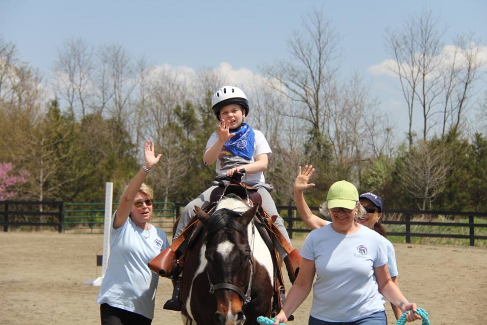 Child on horse at therapeutic riding center with volunteers on each side