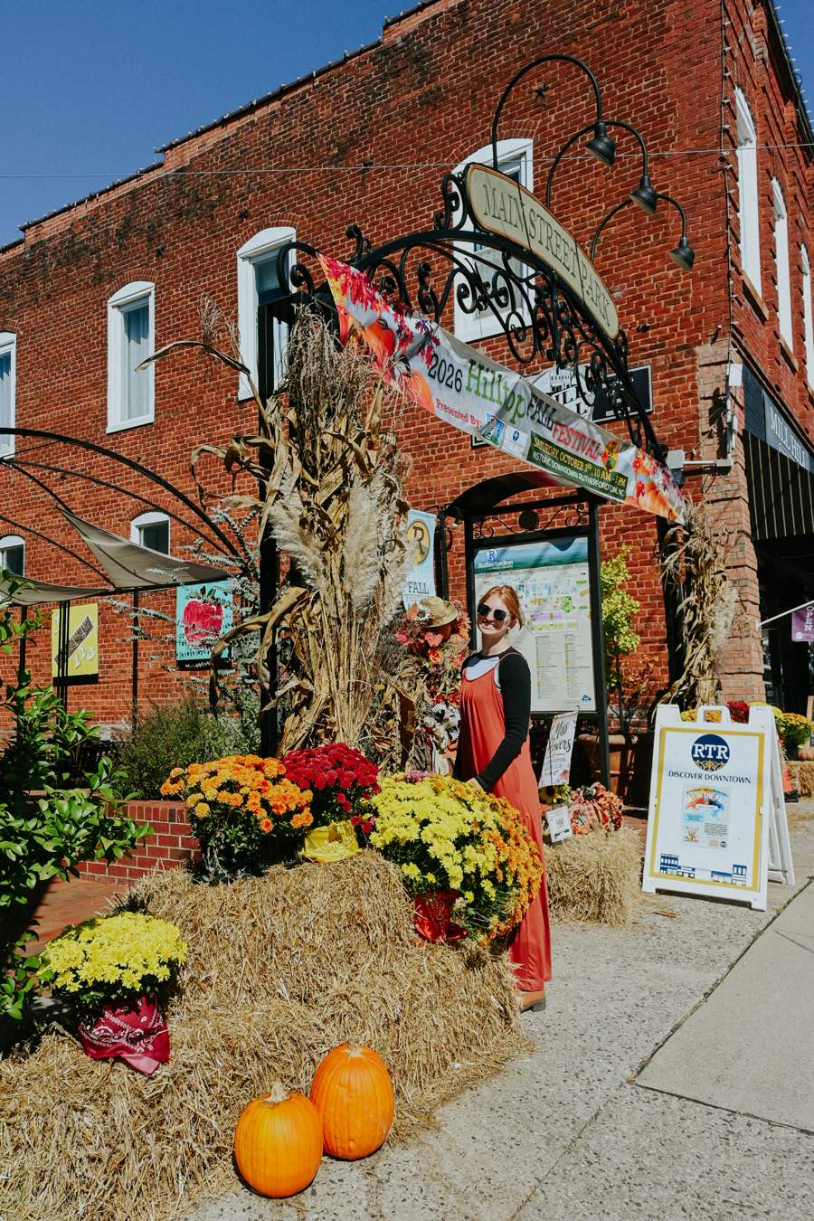 Scarecrows, pumpkins and autumn flowers outside a brick storefront