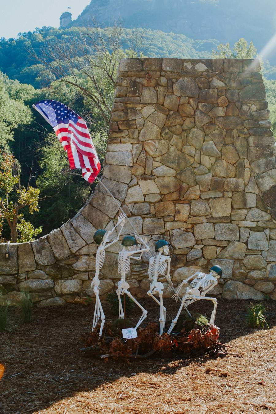 Halloween skeletons beside a stone wall with Chimney Rock in the background