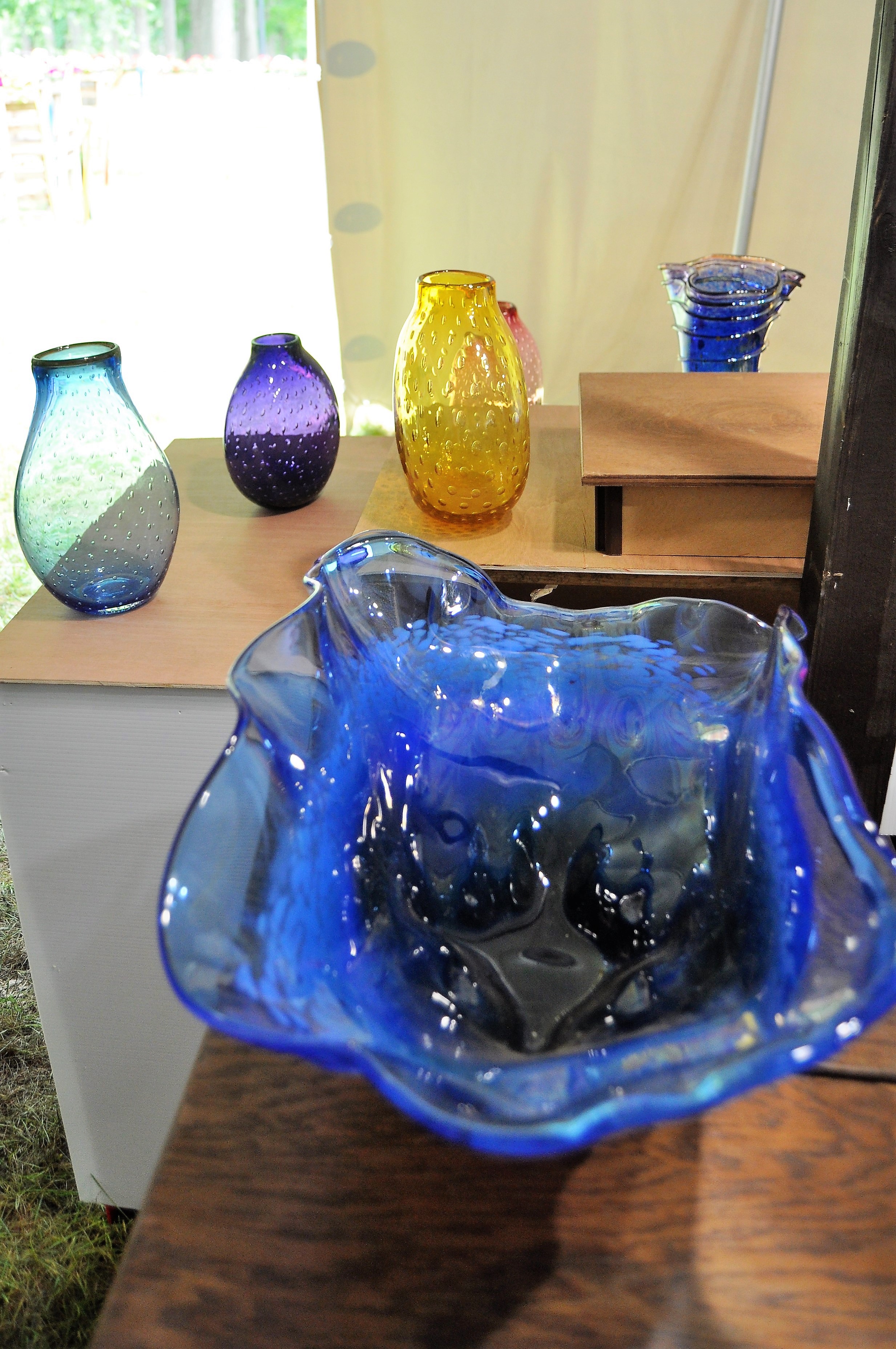 Pieces of glass art work including a large blue bowl with three vases behind it in varying colors