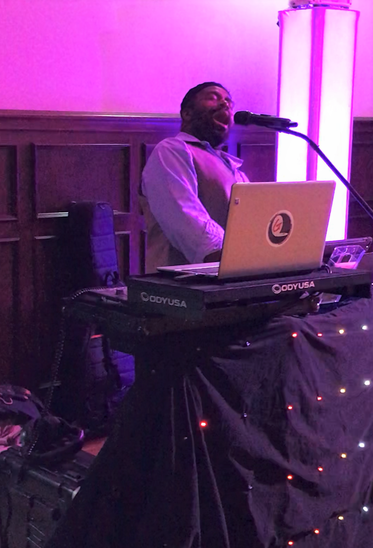 Garland Nelson singing with head thrown back and eyes shut at reception behind a table with tiny white lights and purple lighting