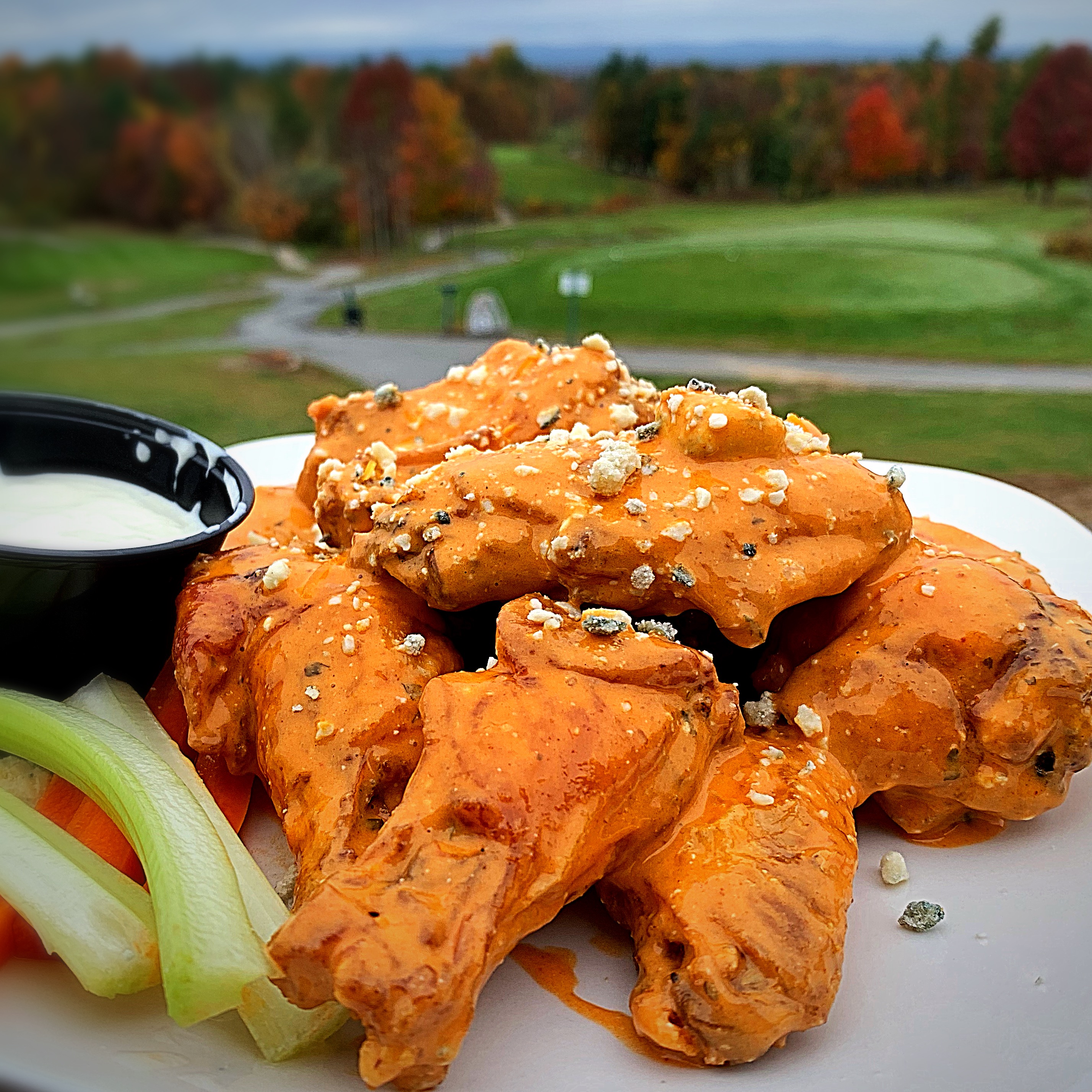 Chicken wings on a white plate with the golf course in the background.