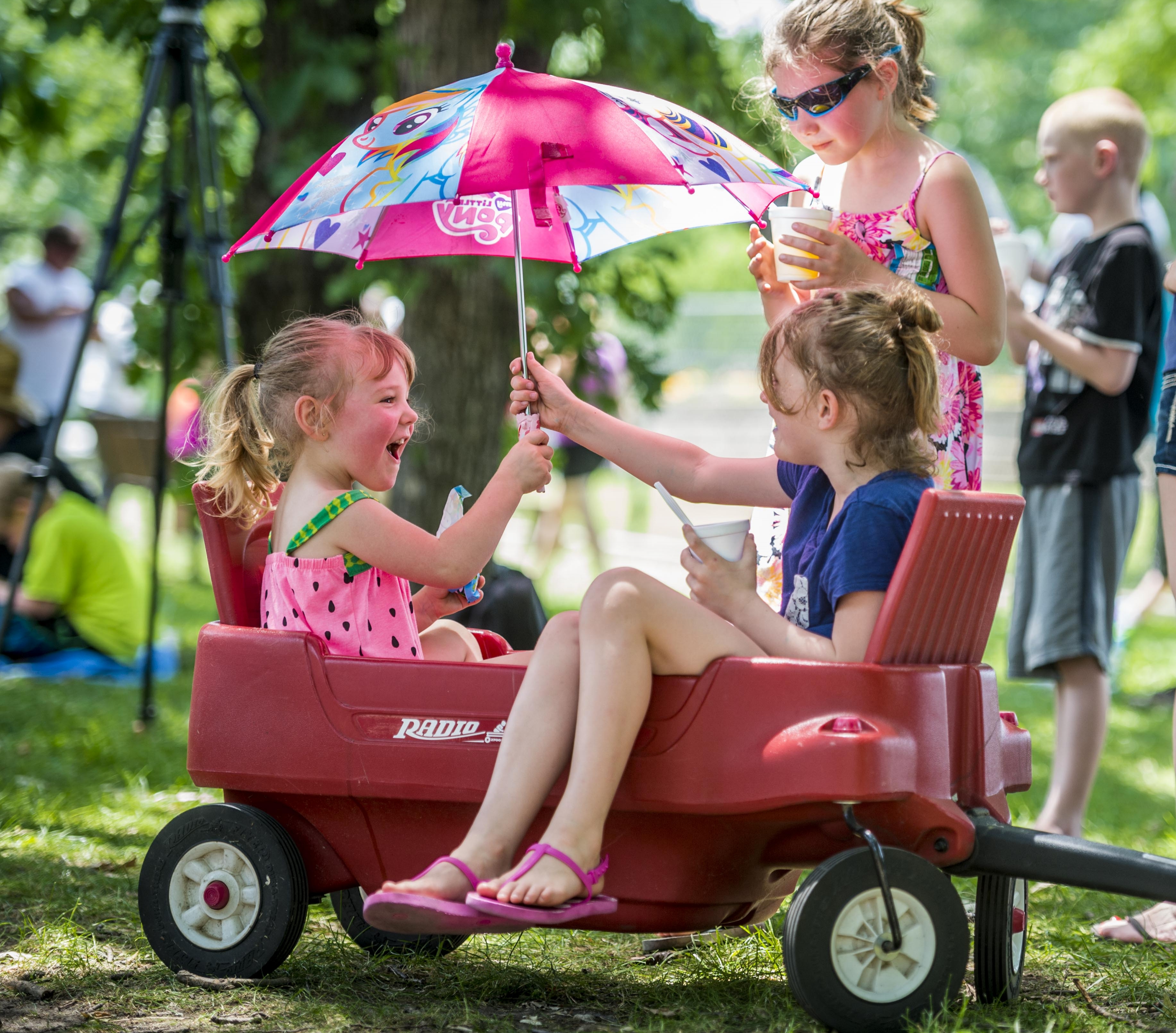 Two girls in a wagon, both holding an umbrella