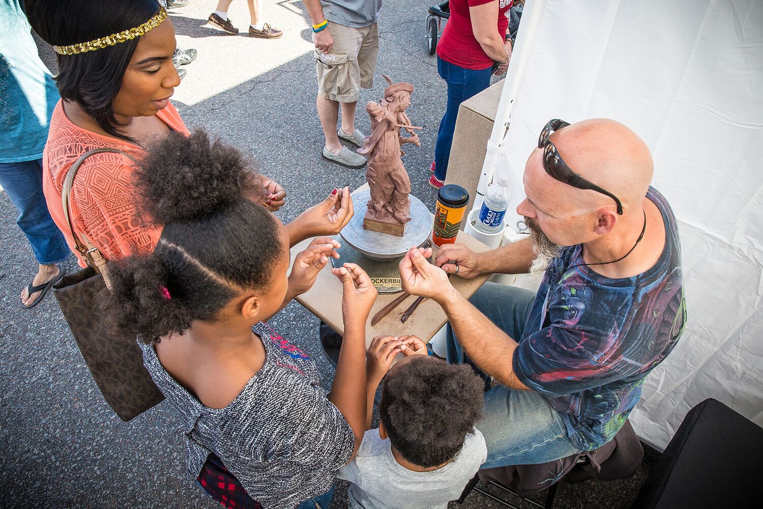 A family interacts with an artist while he creates a small statue out of clay