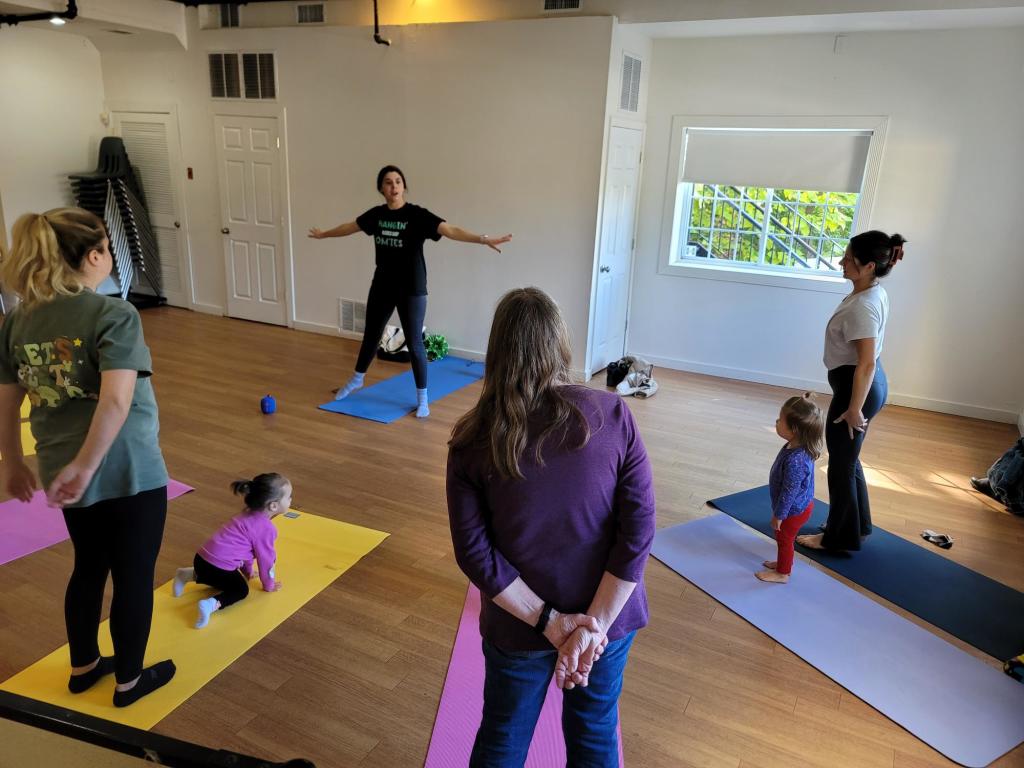 Yoga teacher with families doing yoga at the Mid-Hudson Discovery Museum in Poughkeepsie; the yellow and purple exterior of the museum.