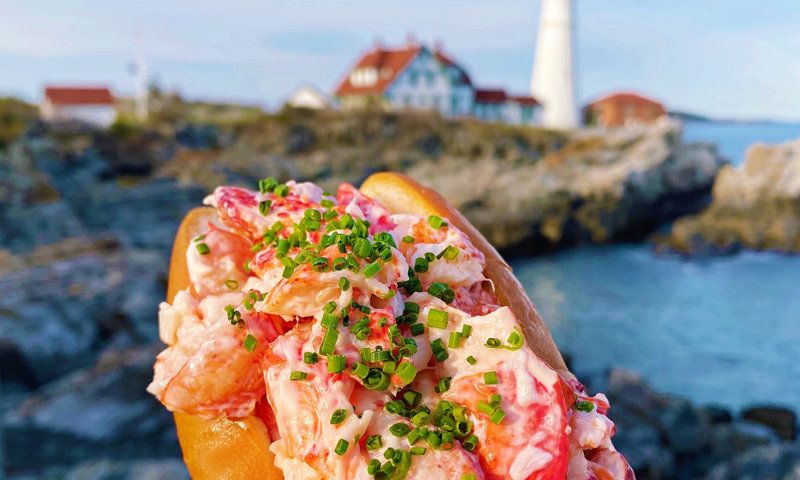 Lobster Roll in front of Portland Head Light. Photo Credit: Bite Into Maine