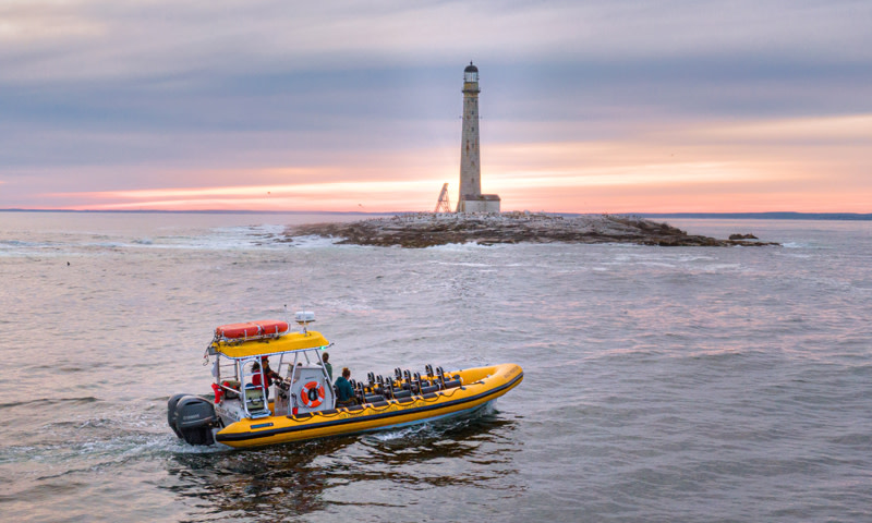 Boat by lighthouse. Photo Credit: New England Eco Adventures