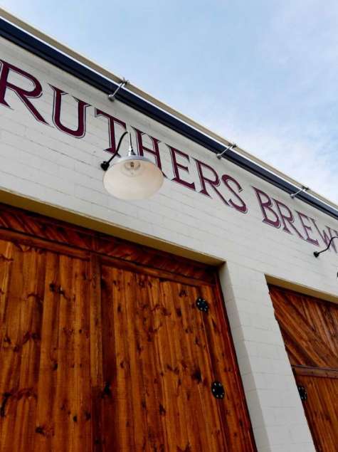 Exterior view of Druthers Brewing Company in Albany with a white brick facade, large wooden barn-style doors, and the brewery’s name painted across the building under mounted exterior lights.