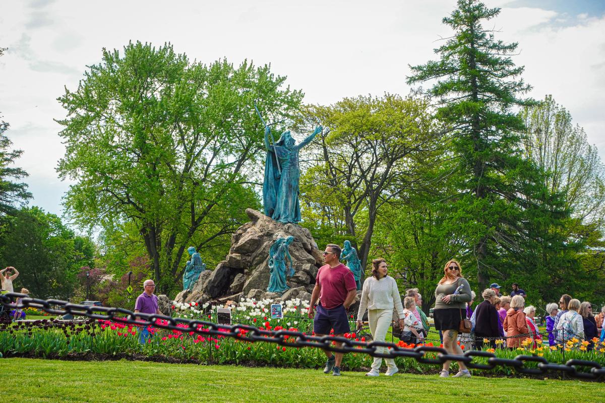 Visitors walk through Washington Park in Albany, NY, near the Moses Fountain surrounded by blooming tulips and green trees during a spring day.