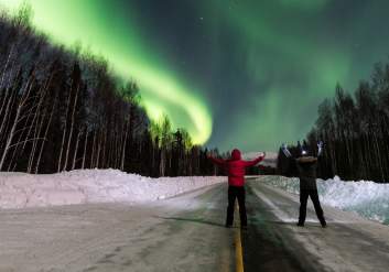 Two people watch the northern lights high overhead as seen from Anchorage.