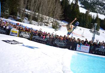 A snowboarder launches through the air in an attempt to cross the icy pond at Alyeska Resort's Spring Carnival and Alaska Airlines Slush Cup.