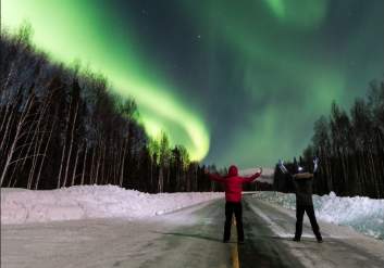Two people stand under the northern lights outside of Anchorage.