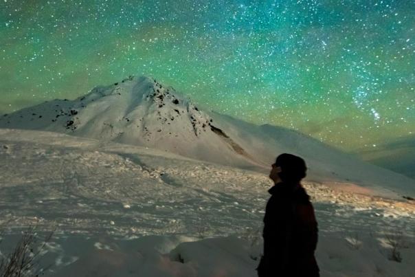 A person gazes at stars and aurora colors on a snowy winter nighttime excursion from Anchorage.