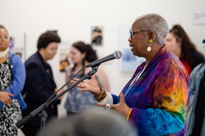 Woman in colorful top speaking into a microphone.