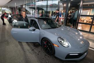 A woman smiles before getting into the passenger side of a gray Porsche for a demo lap at the Porsche Experience Center.