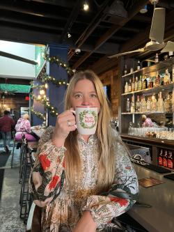 Young woman holding a holiday mug to her lips at the bar of Virgil's Gullah Kitchen & Bar.